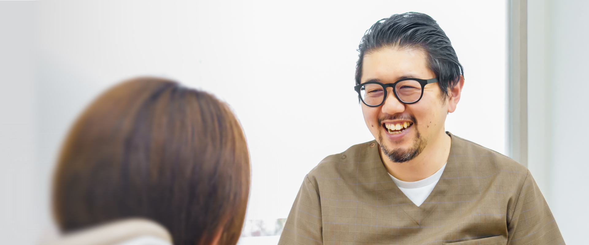 患者と向き合って笑顔で話す眼鏡姿の歯科医師>